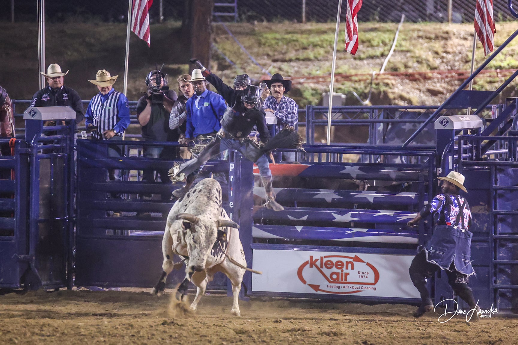 Bull rider leaning back with his free hand high as a white bull bucks out of the chutes at night in Auburn